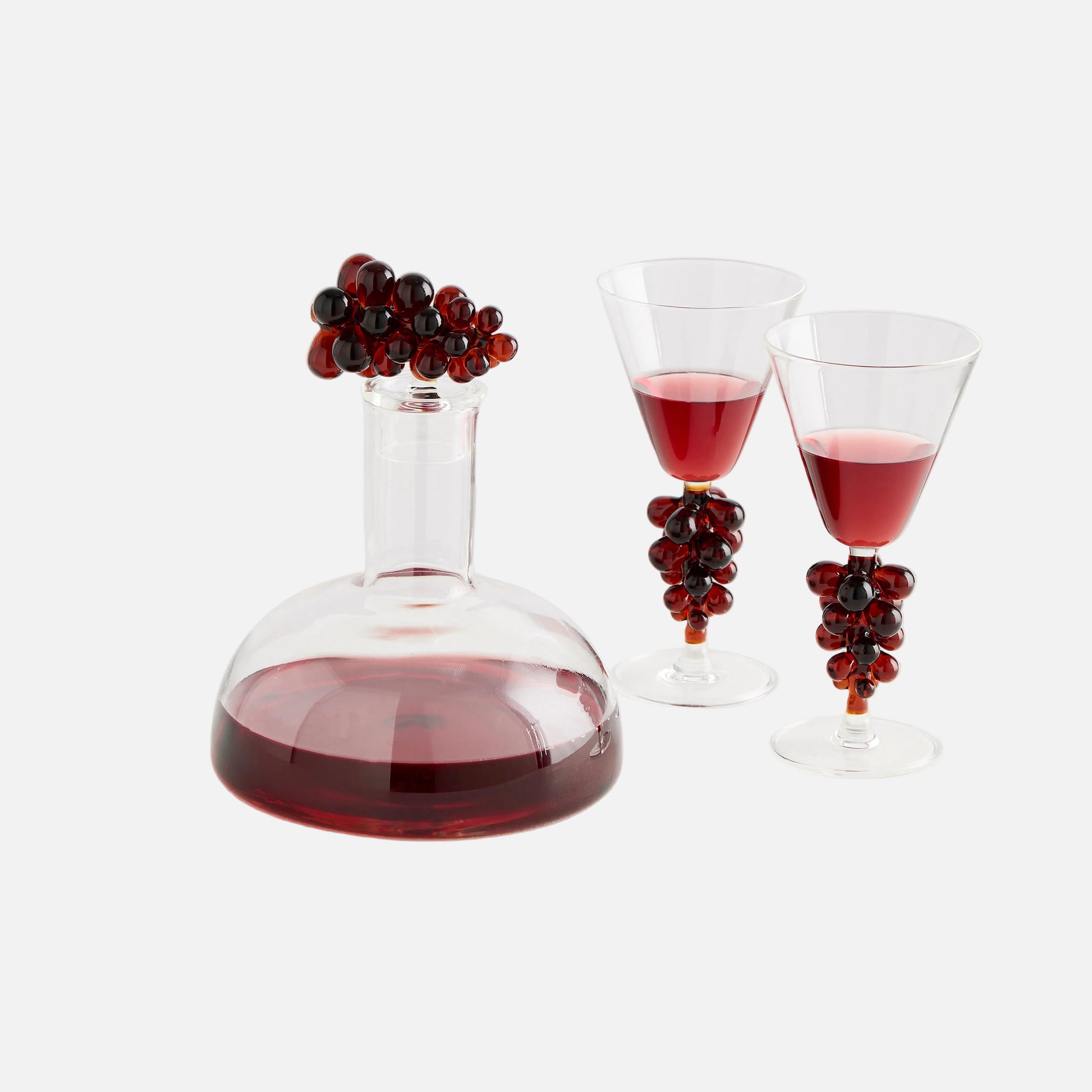 Wine decanter with red wine and two glasses, each with a decorative stem of red grapes on a white background.