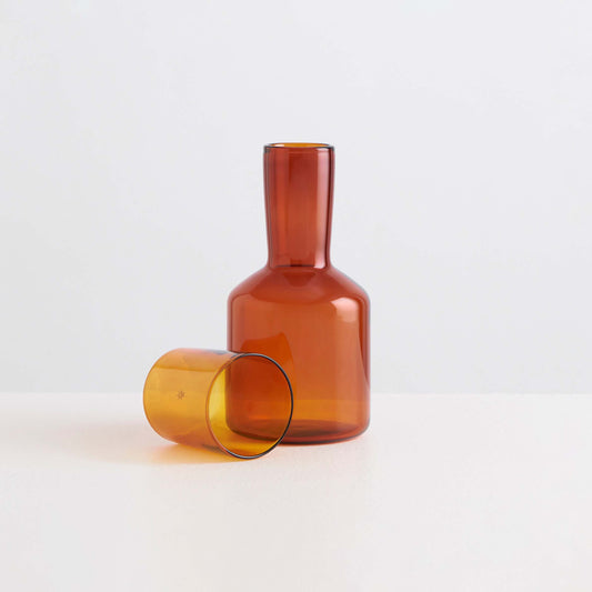 Amber glass carafe and tumbler on a light gray background