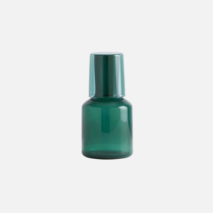 Green glass bottle with a metallic cap on a light gray background