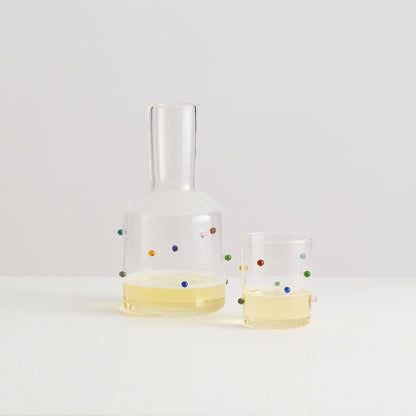 Clear glass carafe and two glasses with colorful dots on a white background