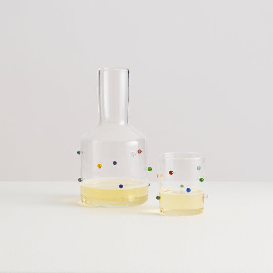 Clear glass carafe and two glasses with colorful dots on a white background