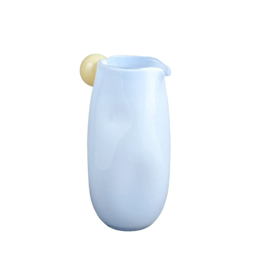 A light blue ceramic pitcher with a small pale yellow spherical accent on the rim, set against a neutral gray studio background.