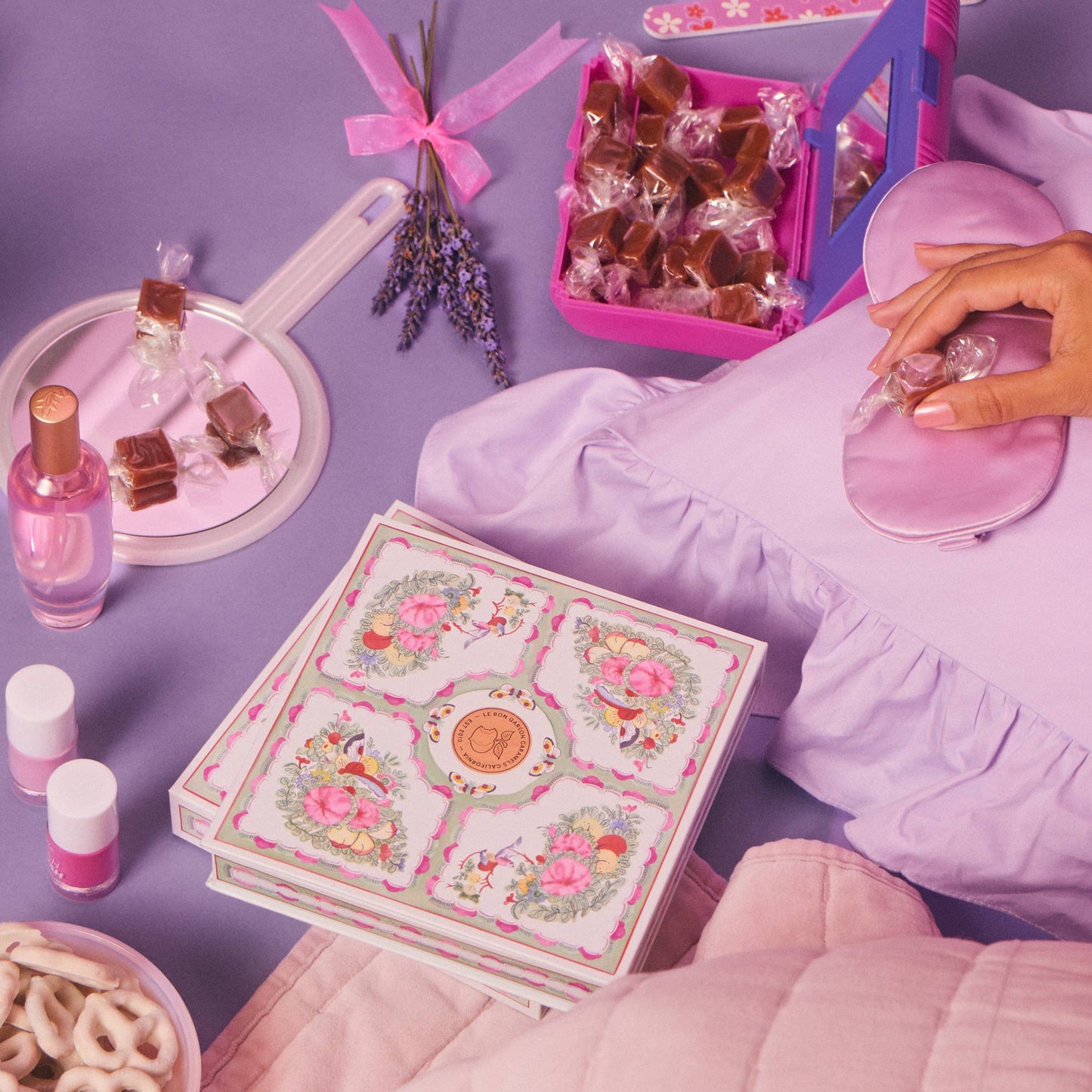 Person sitting on a purple couch with a decorative box, small bottles, and snacks on a matching table.