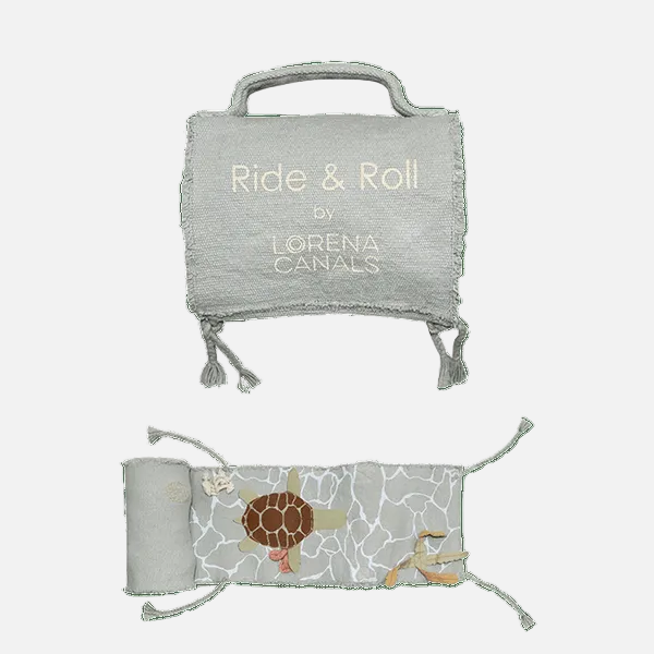 A light gray textured fabric travel pillow set by Lorena Canals, featuring a top view with the embroidered text 'Ride & Roll by Lorena Canals' and a bottom view showing a sea turtle design on a white cracked-glass pattern, set against a solid green background.