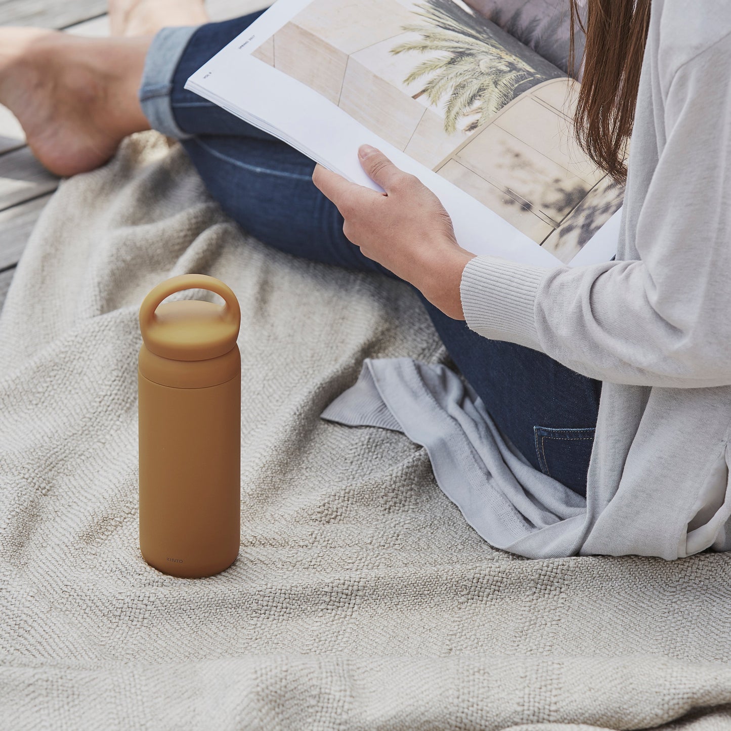 Person reading a book with a mustard yellow water bottle on a blanket