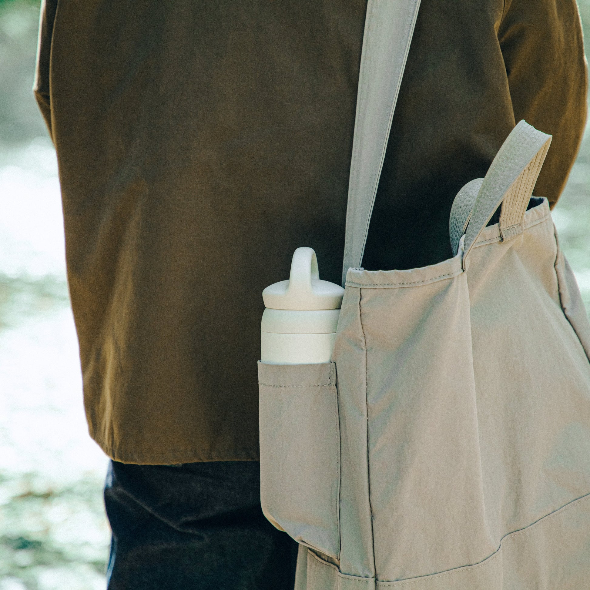 Person wearing a beige apron with a water bottle in a pocket, outdoors.