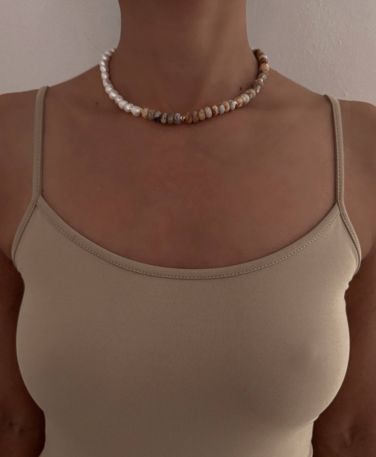Person wearing a beige tank top and pearl necklace against a neutral background