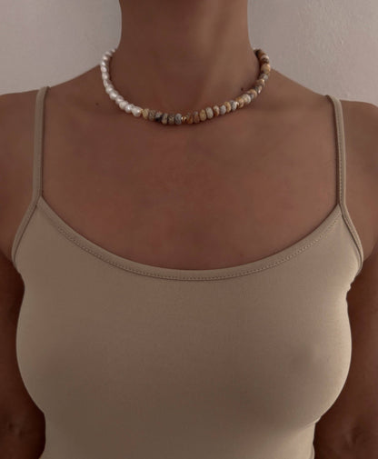 Person wearing a beige tank top and pearl necklace against a neutral background