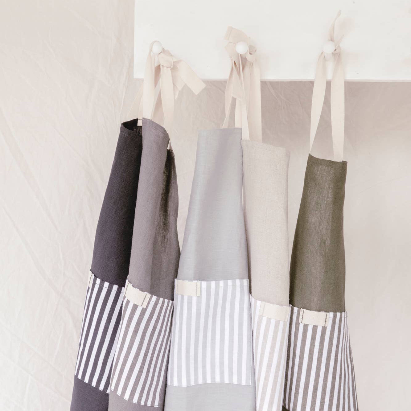 Three aprons with striped patterns hanging on a rack against a white wall.
