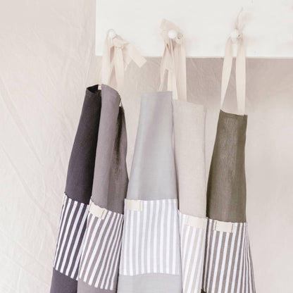 Three aprons with striped patterns hanging on a rack against a white wall.