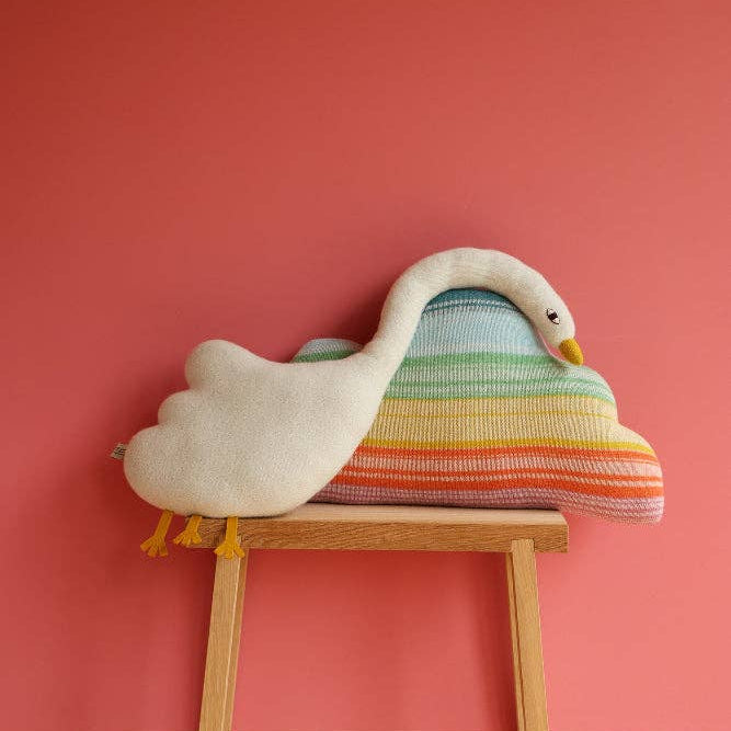 Colorful swan-shaped cushion on a wooden stool against a pink wall