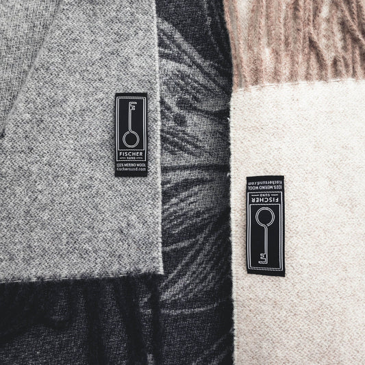 Close-up of a gray and black patterned fabric with a Fischer label, followed by a beige and brown patterned fabric with a Fischer label.