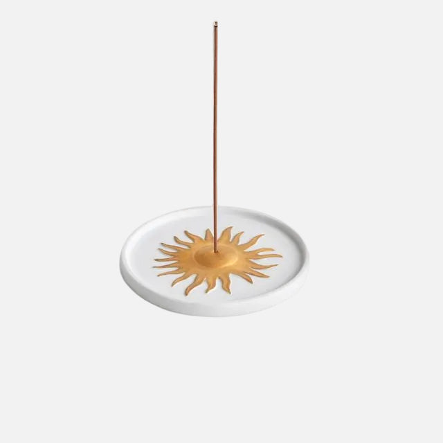 Incense burner with a gold sun design and a single incense stick on a white background