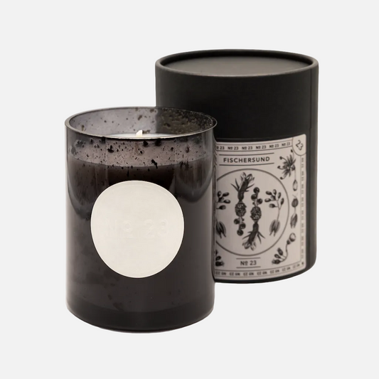 Black candle with decorative label next to its black cylindrical container on a white background