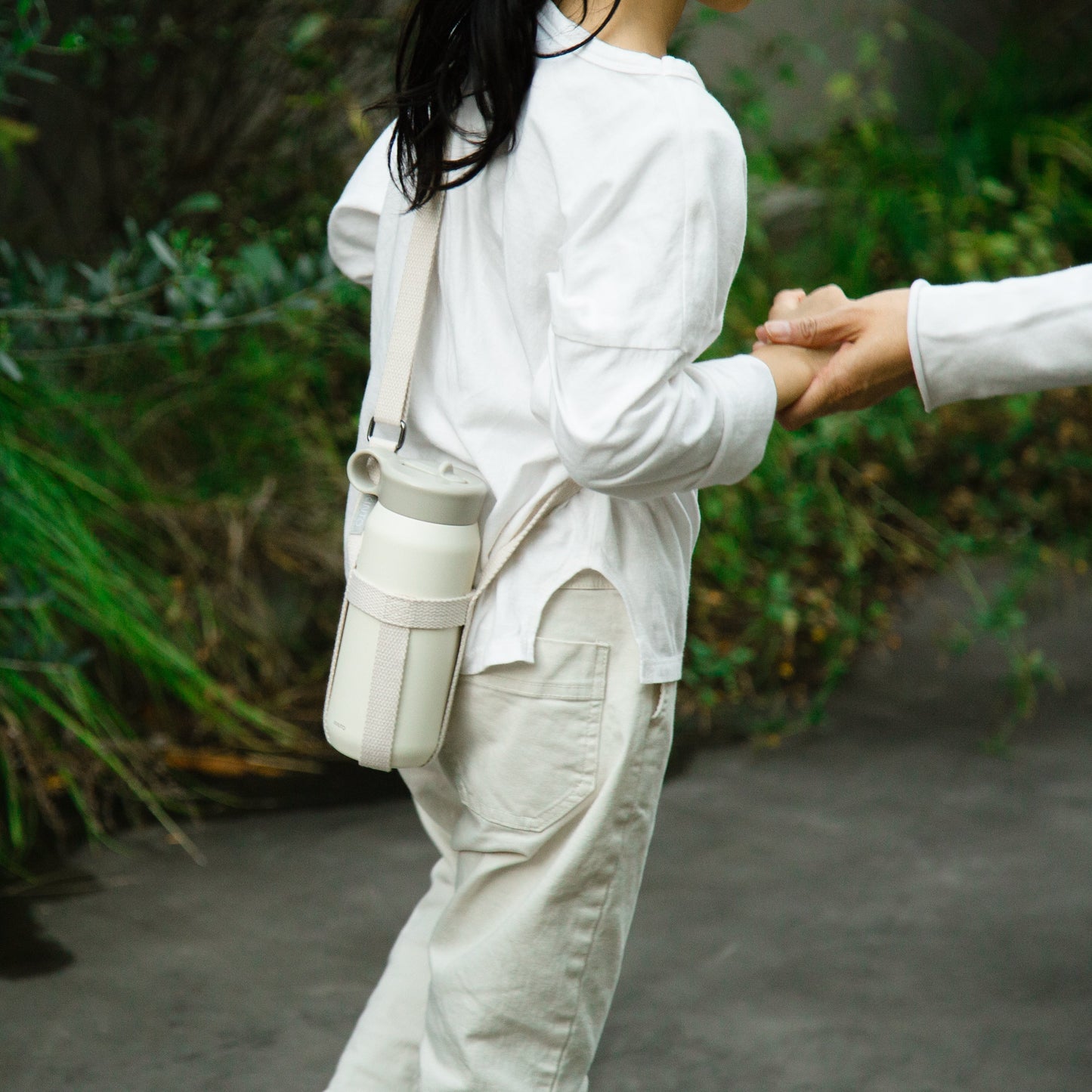 Person wearing a white shirt and beige pants with a beige bag, standing outdoors.