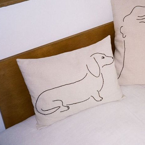 Decorative pillows with line art of a face, dog, and cat on a bed.