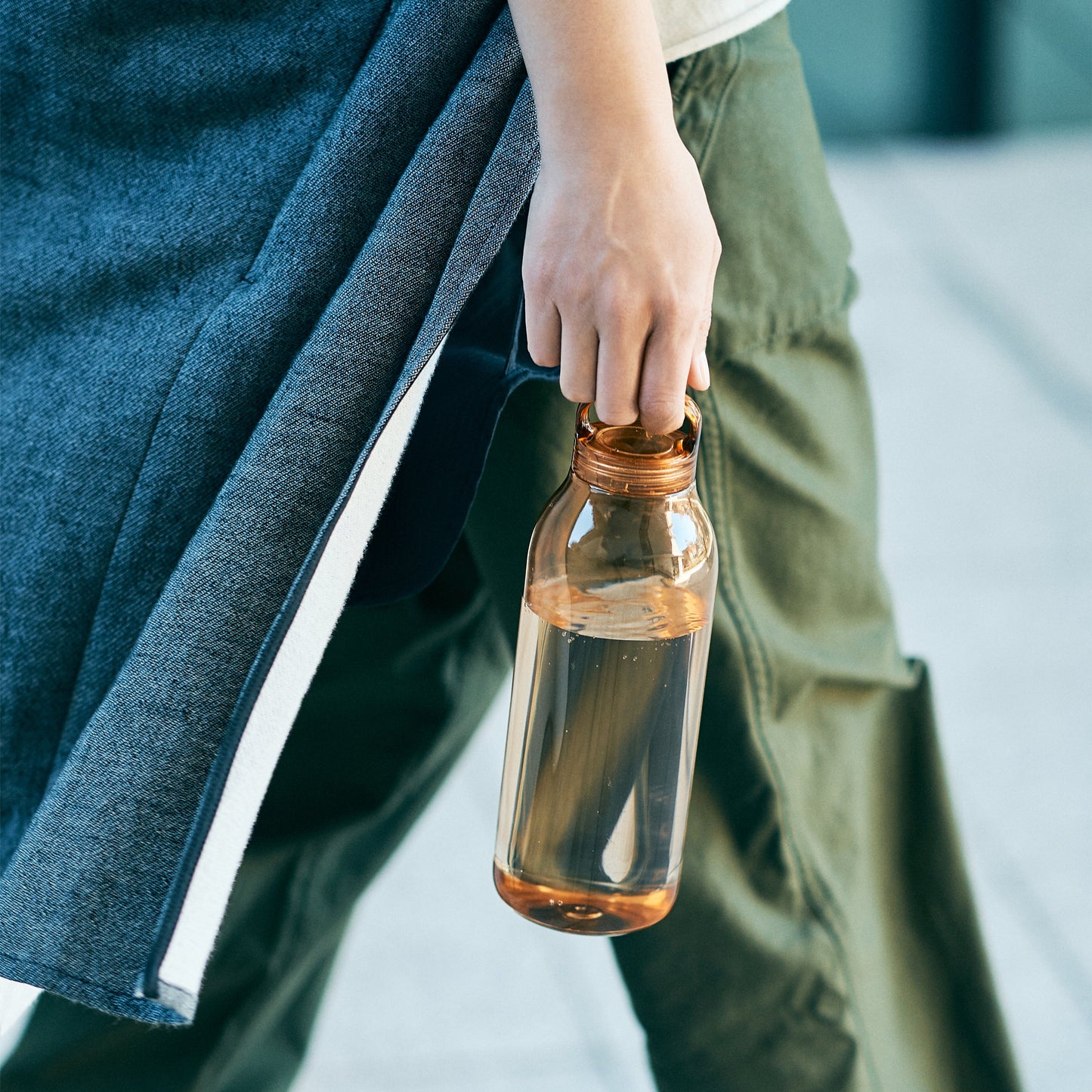 Person holding a clear bottle with a copper cap outdoors
