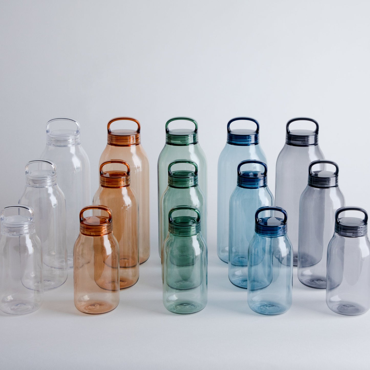 Set of transparent water bottles with colored lids on a light gray background