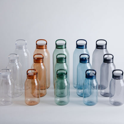 Set of transparent water bottles with colored lids on a light gray background