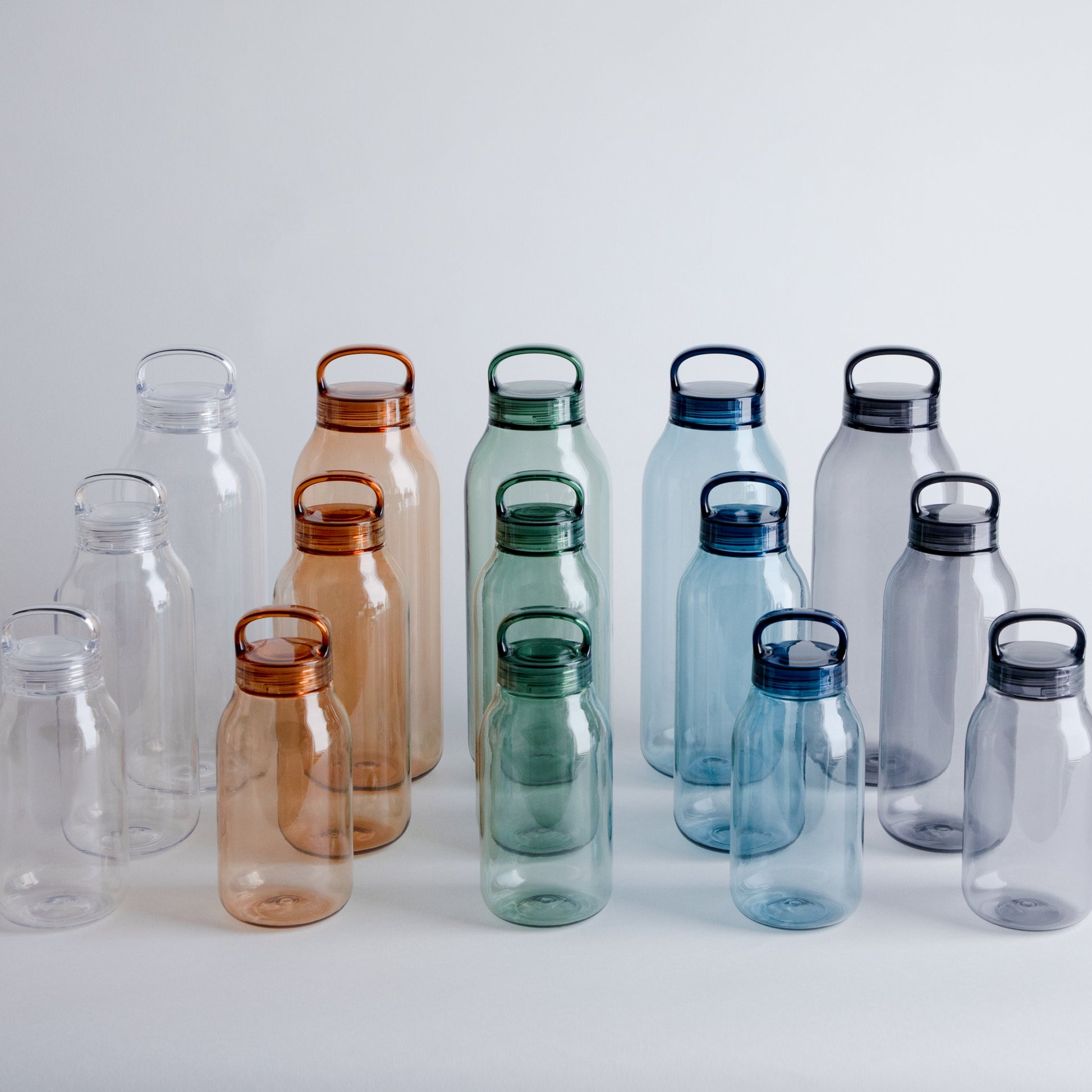 Set of transparent water bottles with colored lids on a light gray background